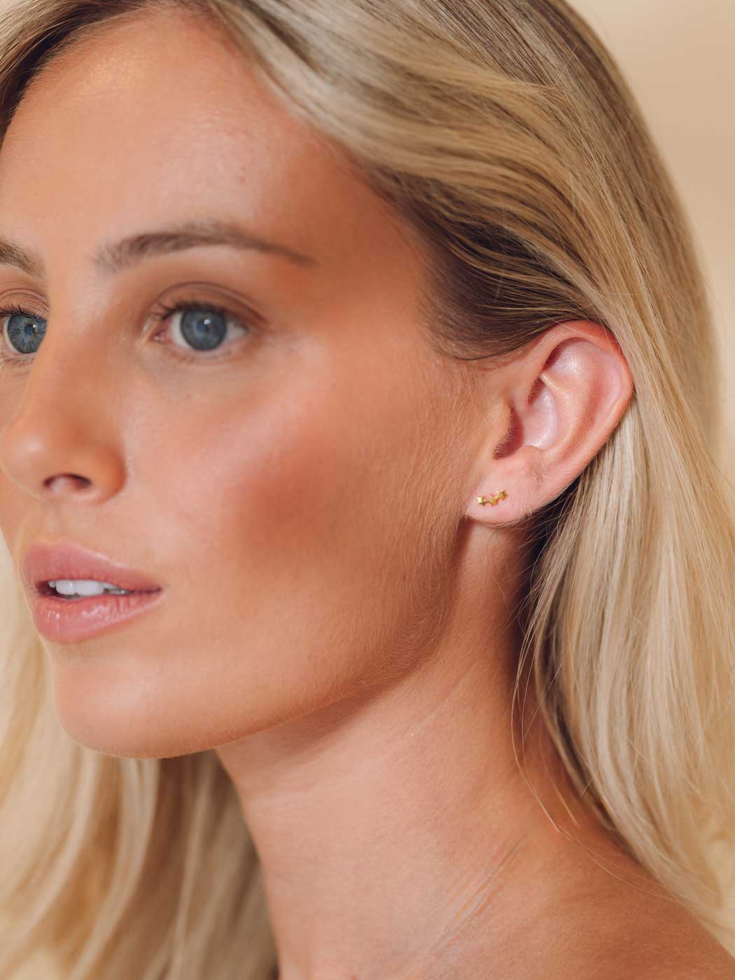 Close-up of a woman wearing a gold star crawler earring with a beige background
