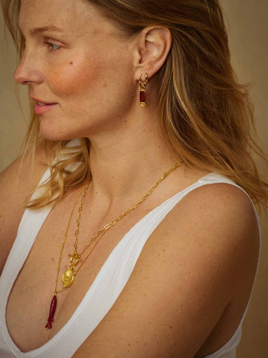 A close-up of a woman wearing gold jewelry, including a unique gold chain necklace with a gold pendant and a carved ruby fish pendant necklace