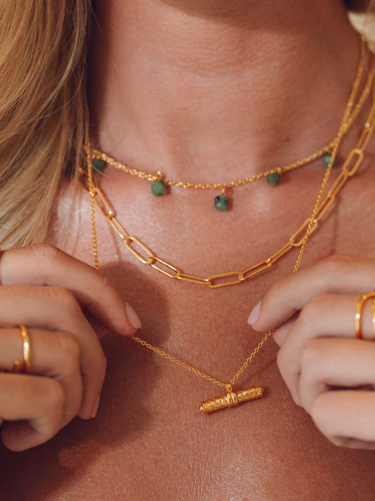 Close-up of a person wearing multiple gold necklaces with green beads.