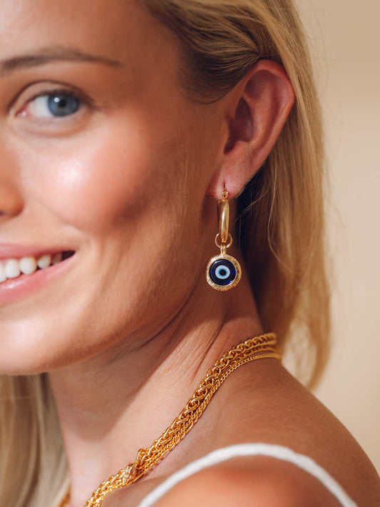 Close-up of a woman wearing gold earrings with a evil eye blue gemstone and matching necklace.