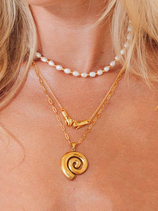 Close-up of a person wearing a gold spiral pendant necklace and a pearl necklace.