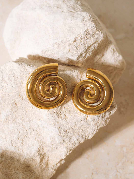 Gold spiral earrings on a textured stone surface