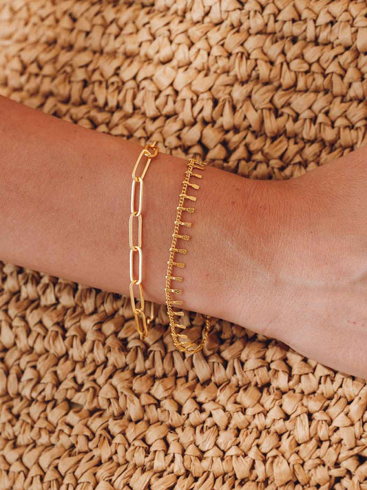 Gold bracelet stack on a wrist against a textured beige background