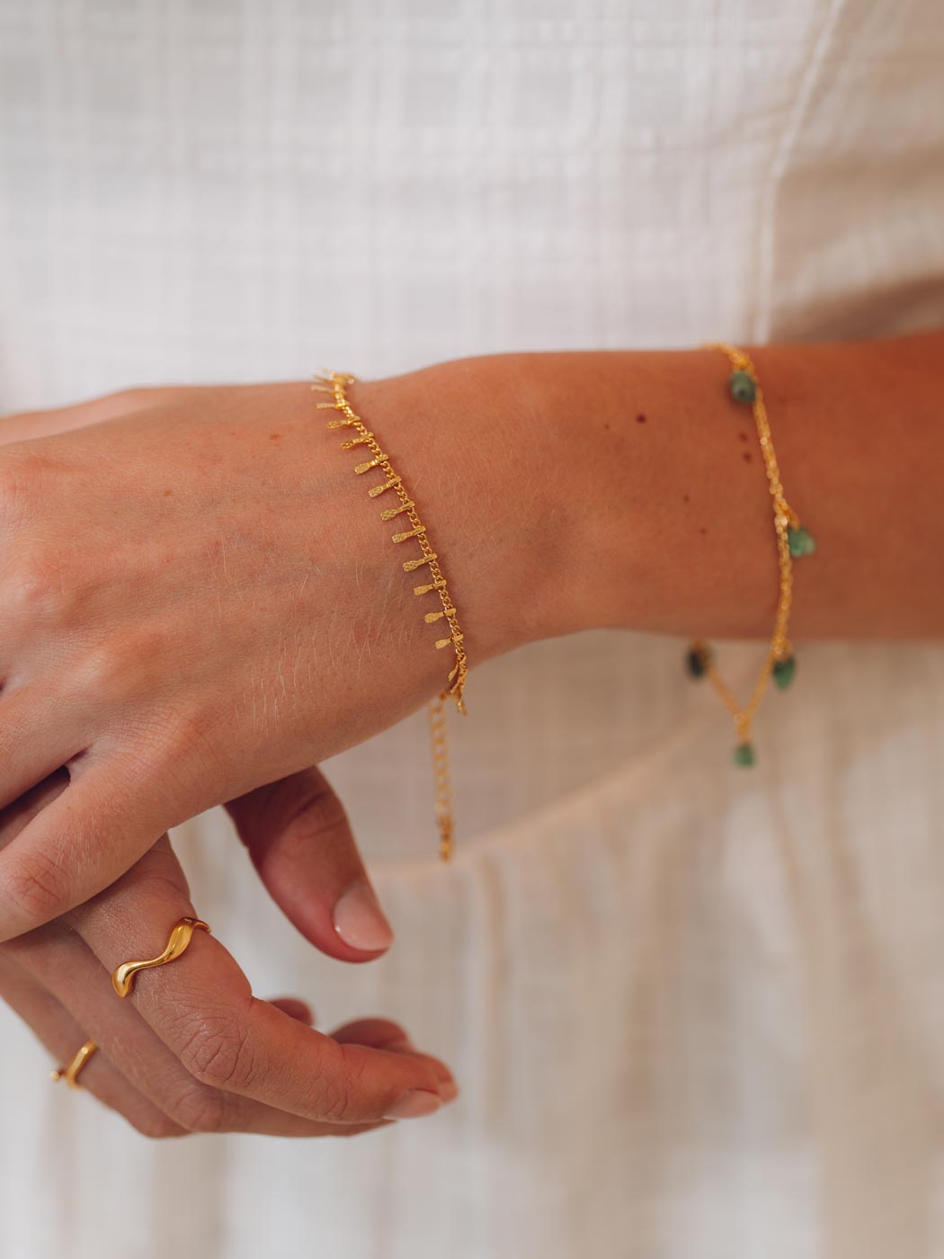 Gold stacked bracelets and rings on a person's wrist against a white background