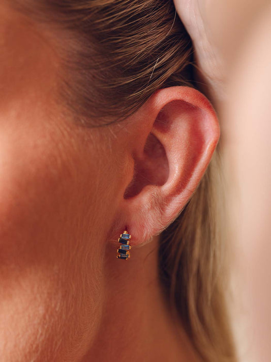 Close-up of an ear wearing a small earring with blue colored sapphire stones.