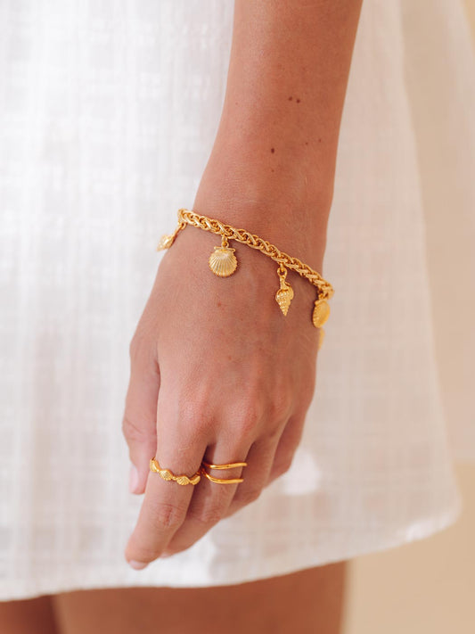 Gold charm bracelet and rings on a person's wrist with a white background