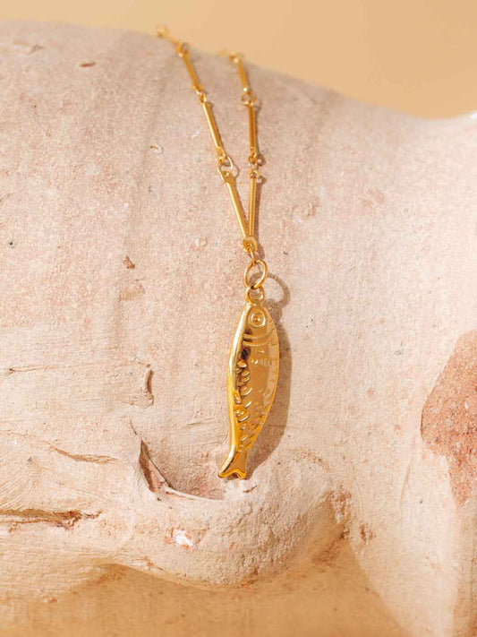 Gold fish-shaped pendant necklace on a stone surface