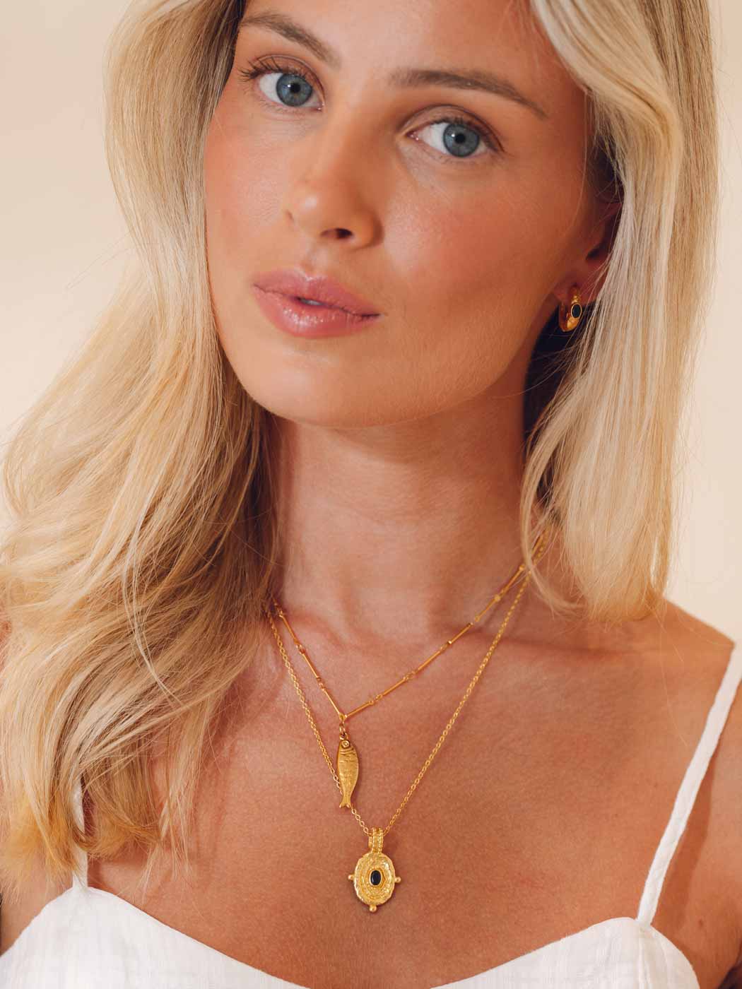 Woman wearing gold necklaces and earrings against a neutral background