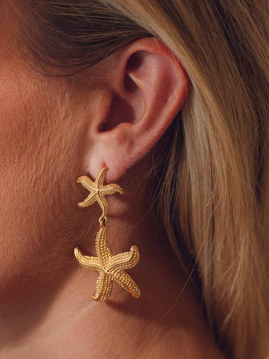 Gold statement starfish drop earrings worn by a person with blonde hair.