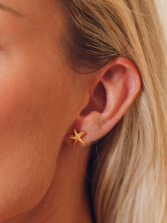 Gold starfish-shaped earring worn by a person with blonde hair.