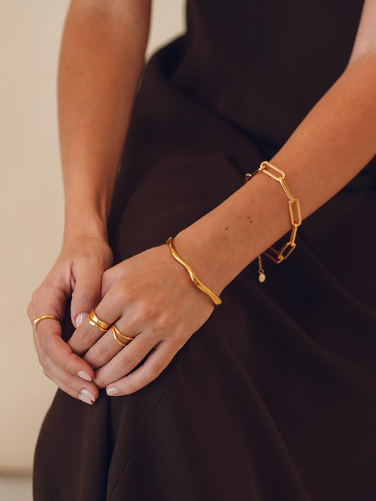 Close-up of a person's hands wearing gold stacking bracelets and rings