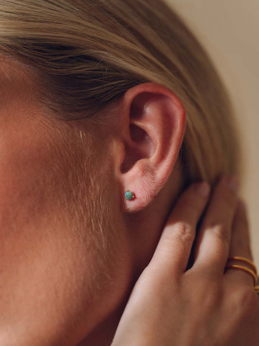 Close-up of an ear with turquoise stud earrings and a hand touching the hair
