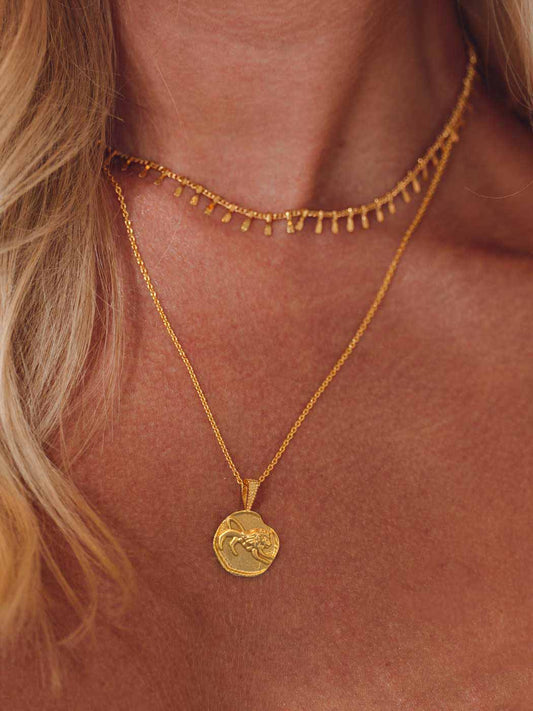Close-up of a person wearing a gold zodiac necklace with a pendant on a neutral background