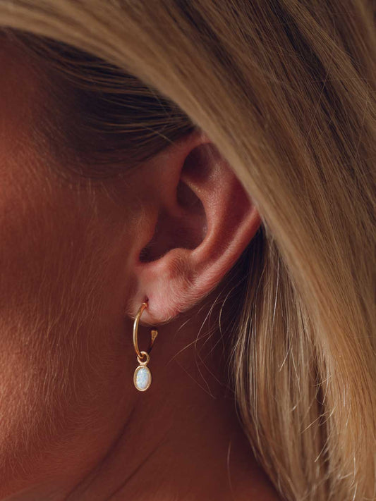 small oval opal pendant on clean gold hoops being worn by blonde model