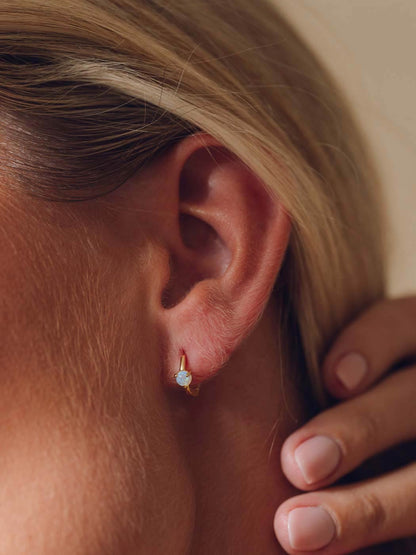 gold huggies with round opal gemstone in center on close up of blonde woman