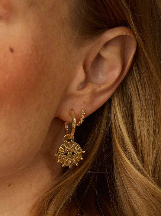 close up of all seeing eye talisman pendant on textured hoops paired with a beaded small huggie in a bohemian style