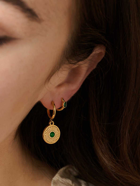 Close-up of a person wearing gold hoop earrings with green gemstones.