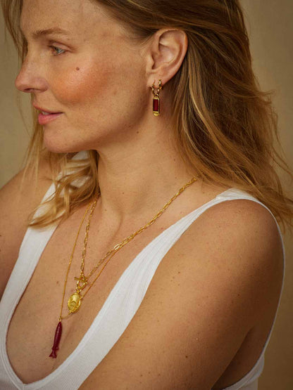 A close-up of a woman wearing gold jewelry, including a unique gold chain necklace with a gold pendant and a carved ruby fish pendant necklace
