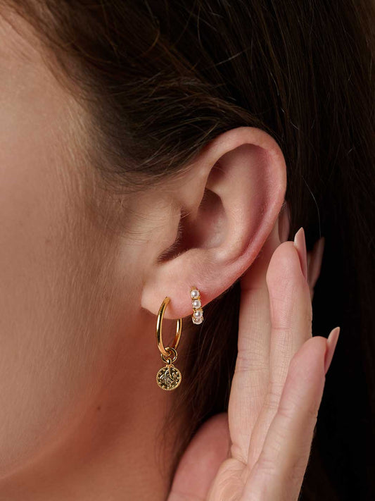 Close-up of an ear wearing gold pearl hoop huggies with a dark background
