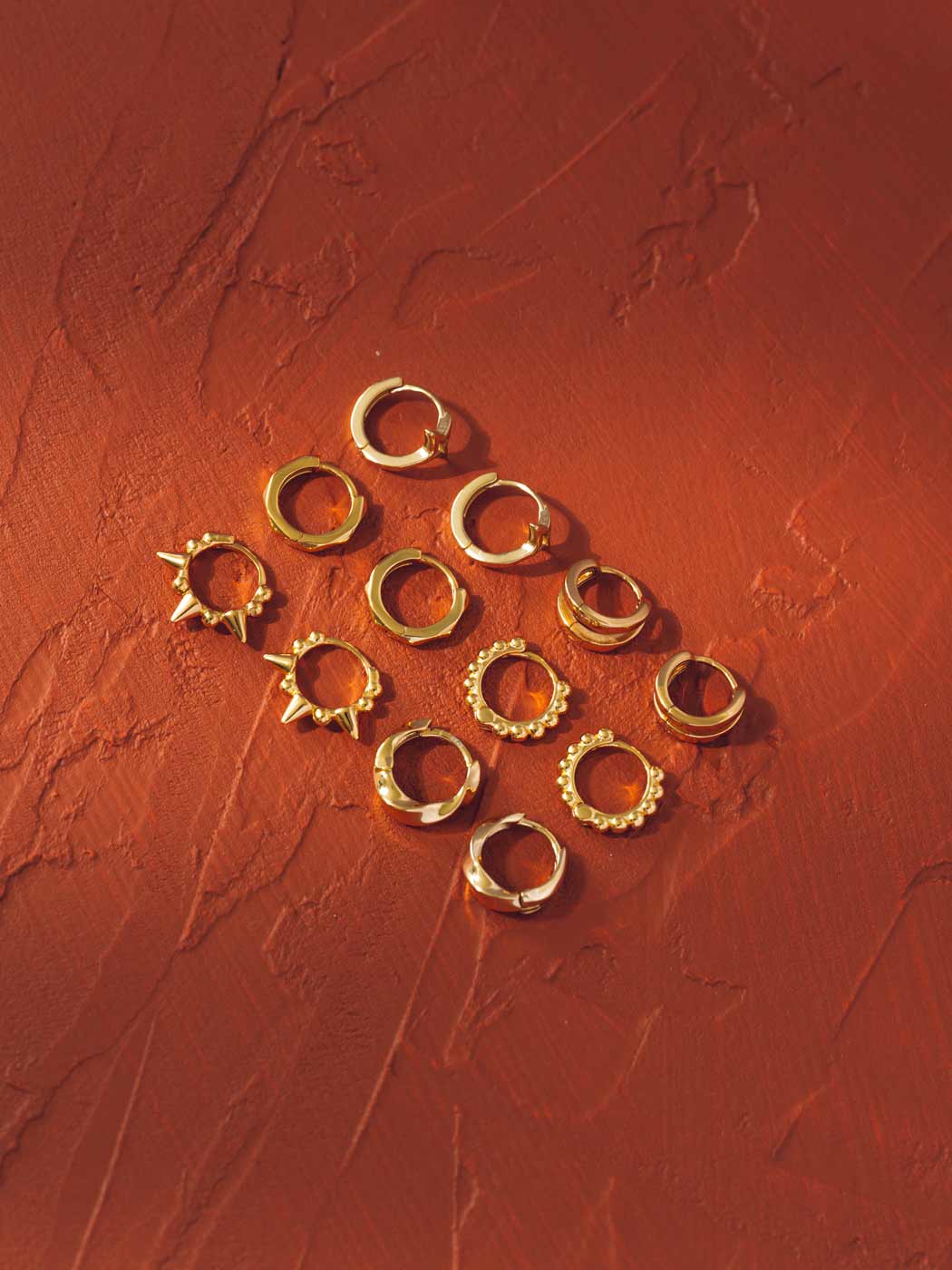Gold huggie hoop earring range on a textured red surface
