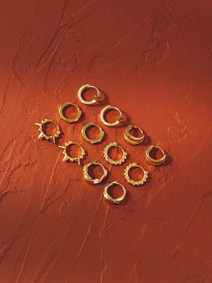 Gold huggie hoop earring range on a textured red surface