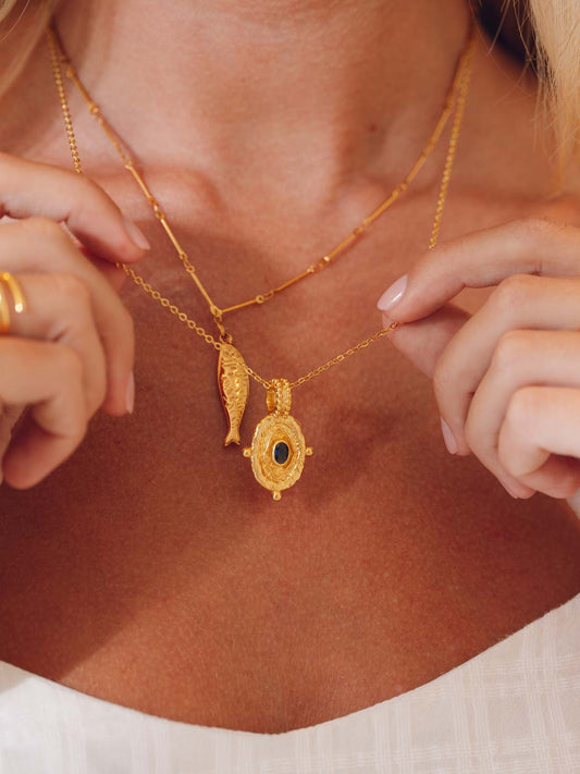 Gold necklace with pendant worn by a person, close-up on neck and chest.