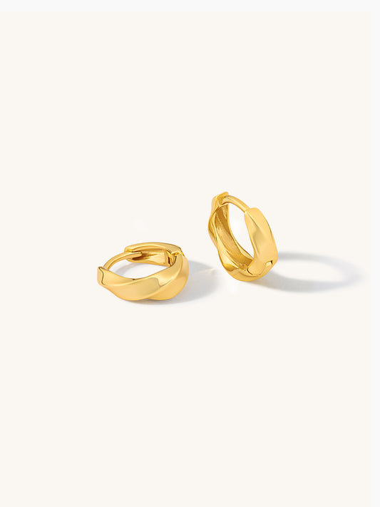 Pair of gold twisted huggie earrings on a white background