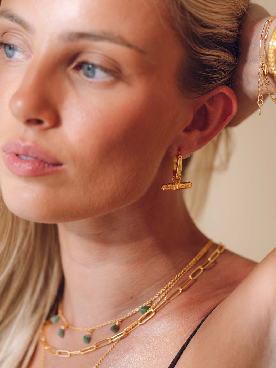 Close-up of a woman wearing gold earrings and necklaces against a neutral background