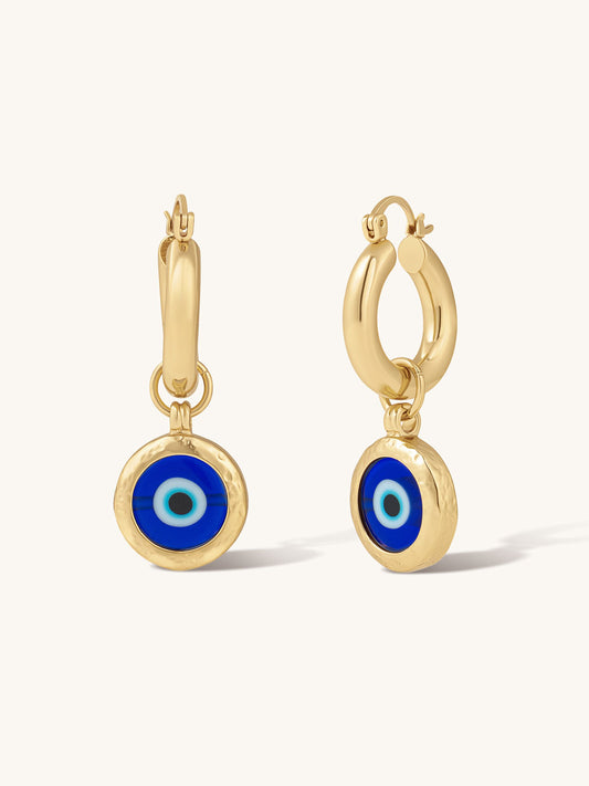 Gold statement hoop earrings with blue evil eye charms on a white background
