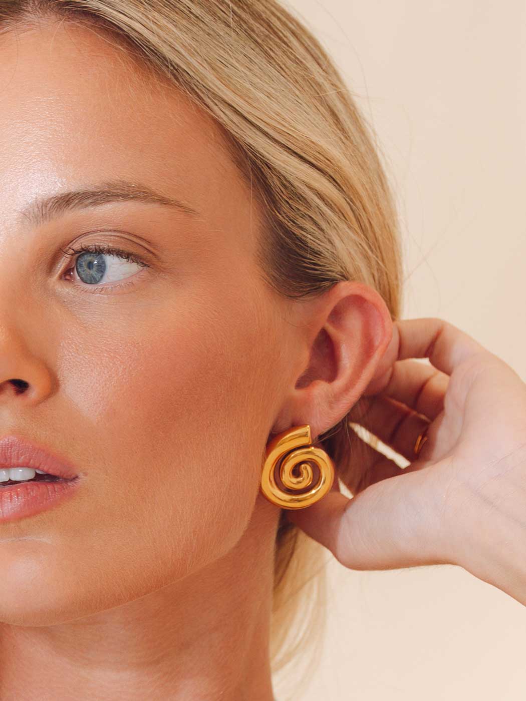 Close-up of a woman wearing a gold spiral earring against a beige background