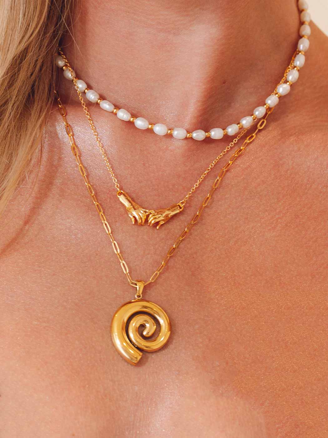 Close-up of a person wearing two gold necklaces with spiral pendant and a pearl choker