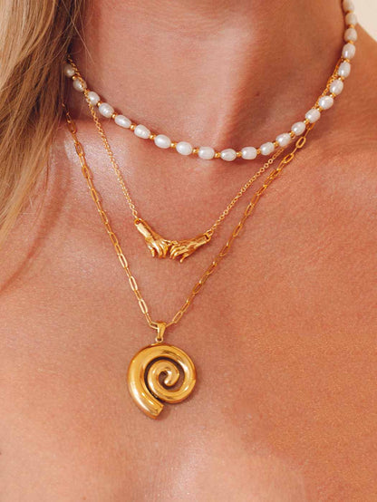 Close-up of a person wearing two gold necklaces with spiral pendant and a pearl choker
