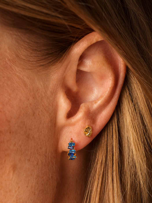 Close-up of an ear wearing a gold nugget stud earring with some sapphire huggies