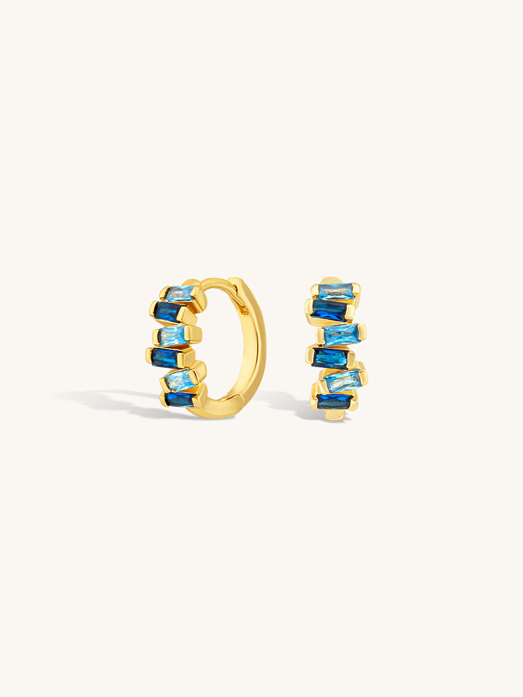 Gold huggie earrings with sapphire blue gemstones on a white background
