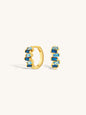 Gold huggie earrings with sapphire blue gemstones on a white background