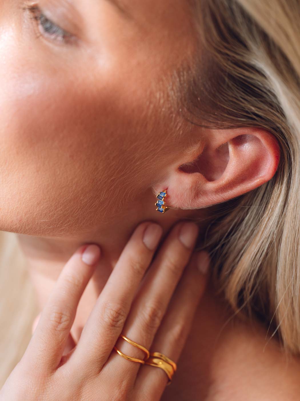 Close-up of a person wearing a gold ring and colorful sapphire earring.