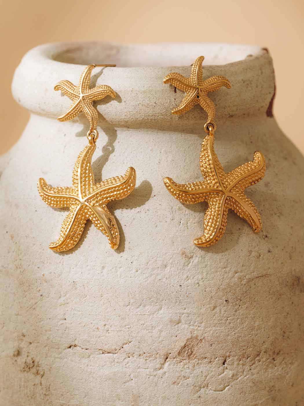 Gold starfish earrings on a textured beige surface