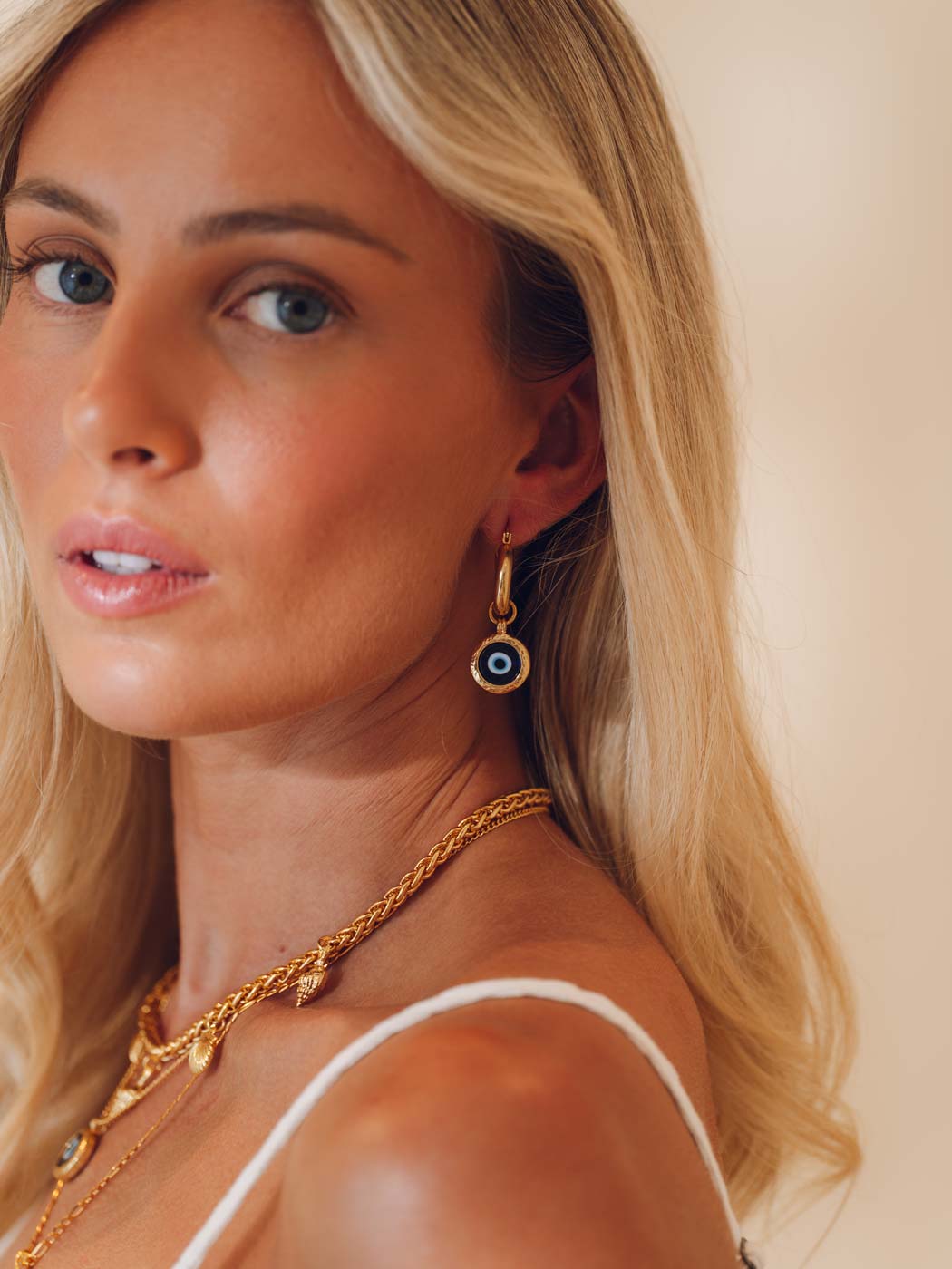 Woman wearing gold evil eye statement hoops with a neutral background