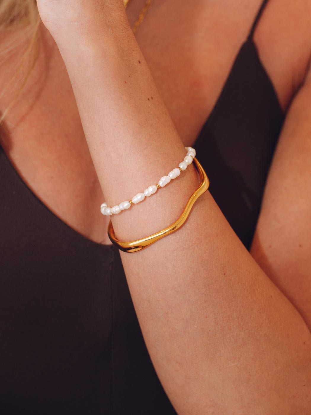 Gold irregular shaped cuff bracelet and pearl bracelet on a person's wrist 
