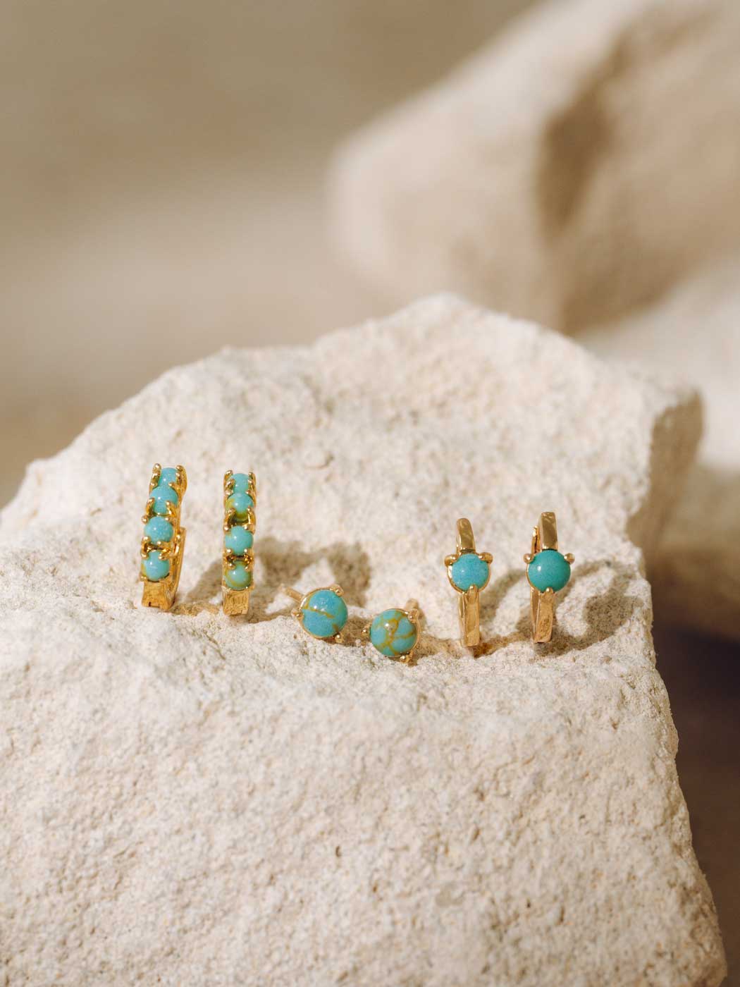 Gold and turquoise earrings on a textured surface