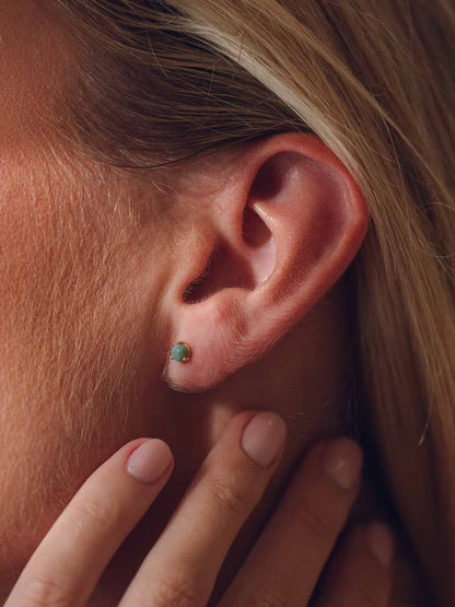 Close-up of an ear with a turquoise stud earring, hand touching the earlobe