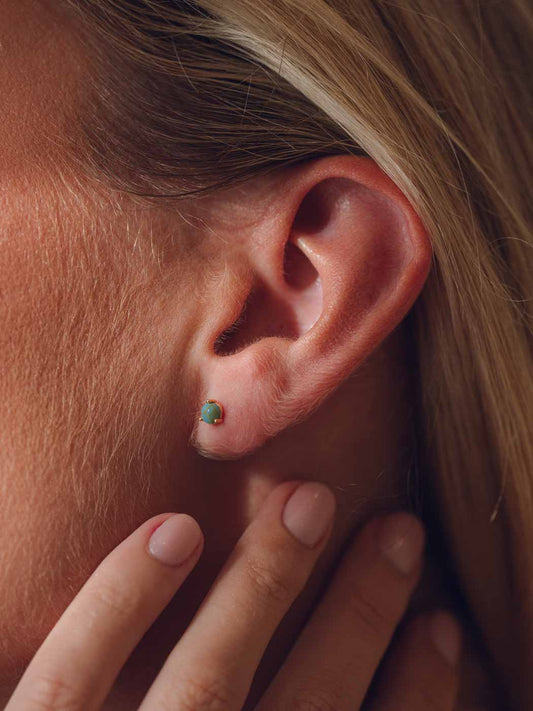 Close-up of an ear with a turquoise stud earring, hand touching the earlobe