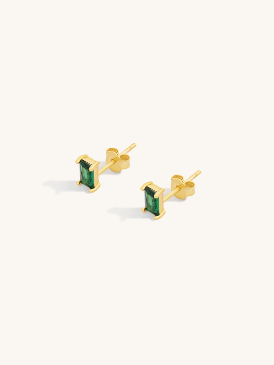 Gold earrings with green faceted emerald gemstones on a white background