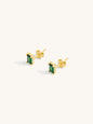 Gold earrings with green faceted emerald gemstones on a white background