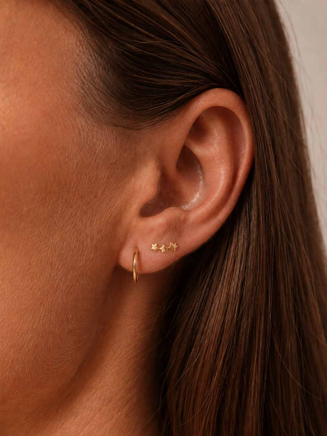 Close-up of an ear wearing gold hoop and star-shaped earrings with brown hair.