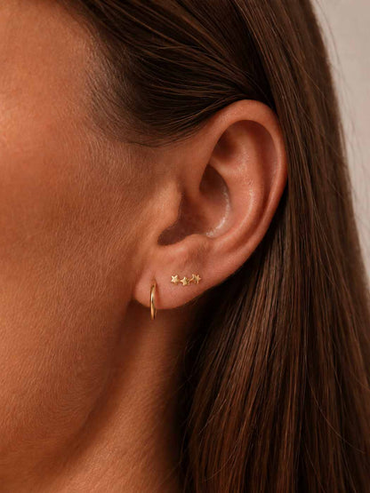 Close-up of an ear wearing gold hoop and star-shaped earrings with brown hair.