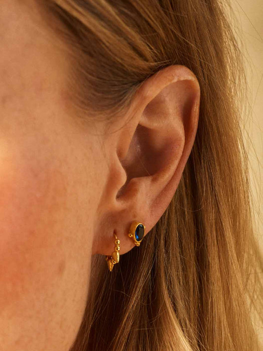 Close-up of an ear wearing gold earrings with a blue sapphire gemstone.
