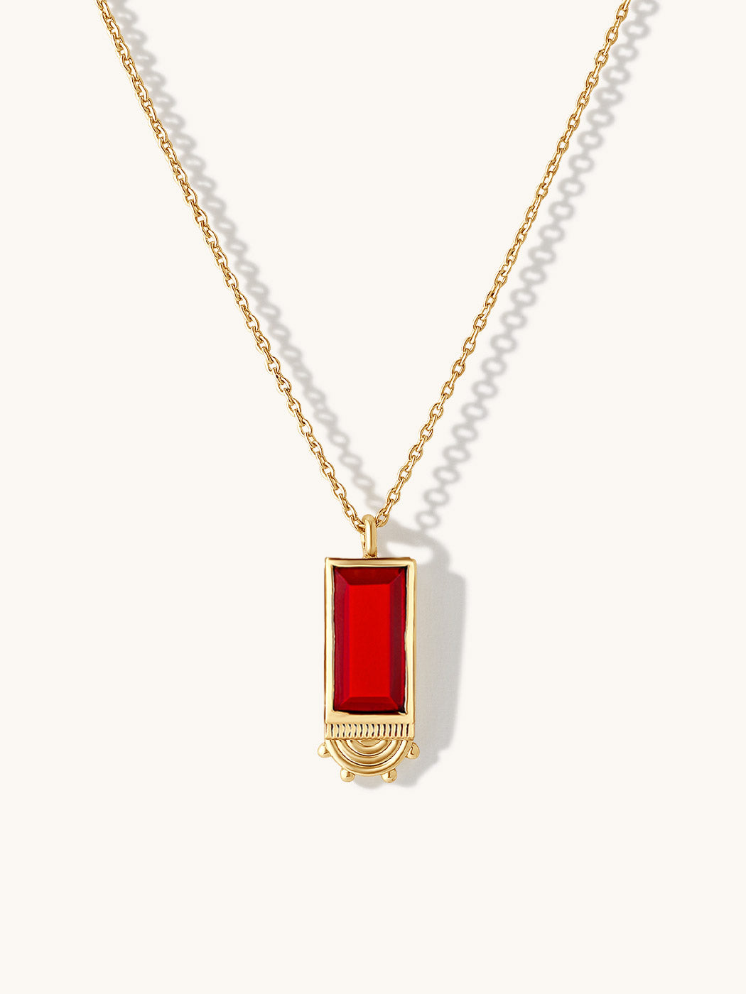 A gold chain necklace with a rectangular ruby gemstone pendant, displayed on a clean off-white background with soft shadows.