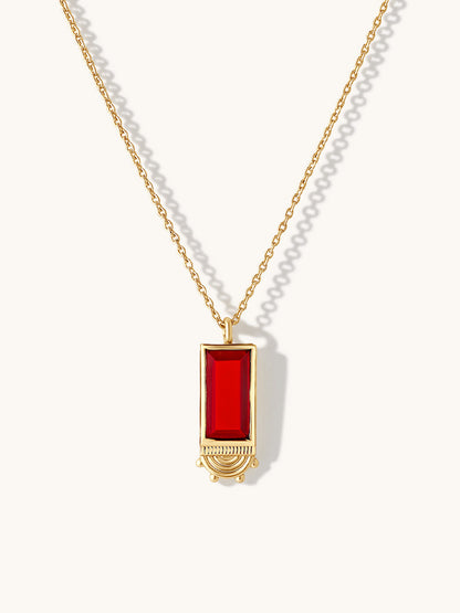 A gold chain necklace with a rectangular ruby gemstone pendant, displayed on a clean off-white background with soft shadows.