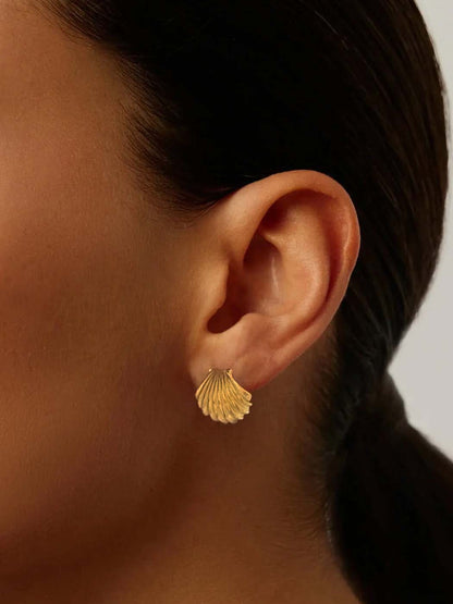 Gold shell earring worn by a person with a neutral background